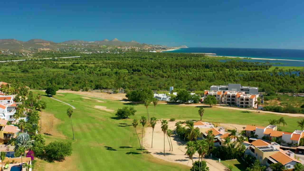 Aerial golf course foreground with homes, trees, ocean, and hills.
