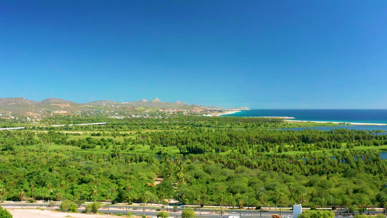 San Jose Del Cabo aerial frame with more open sky above a green valley, lagoon-like water, blue ocean, distant hills, and no visible people.