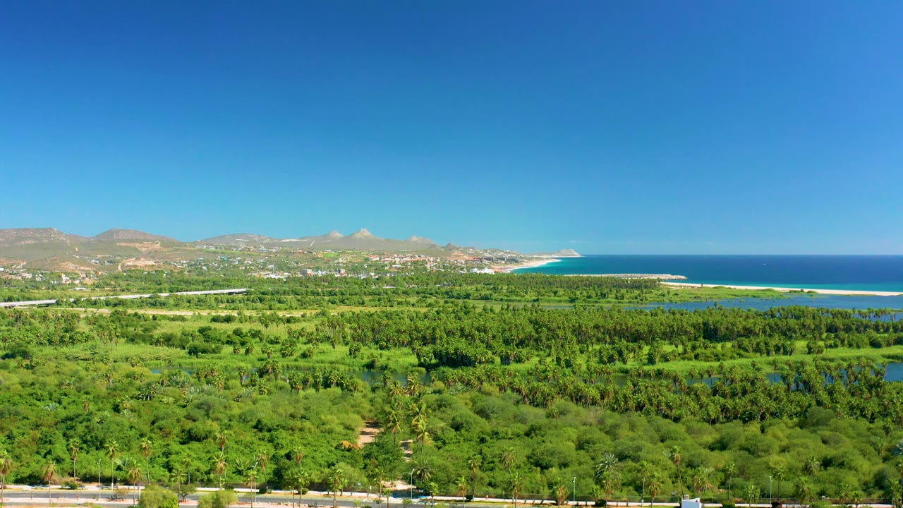Aerial landscape with green valley, small water areas, distant town edge, and ocean.