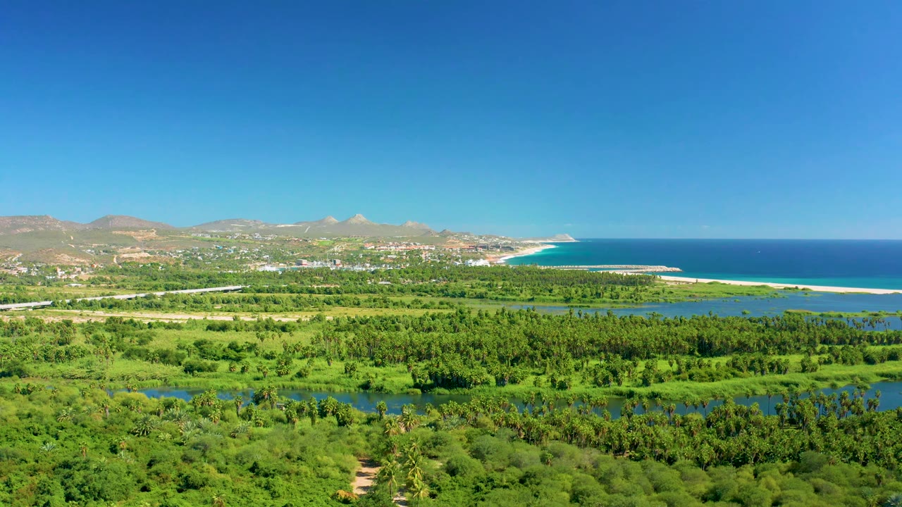 Third frame shows San Jose Del Cabo from above with a broad green valley, lagoon-like river water, a light sand beach, blue ocean, distant hills, and no visible people.