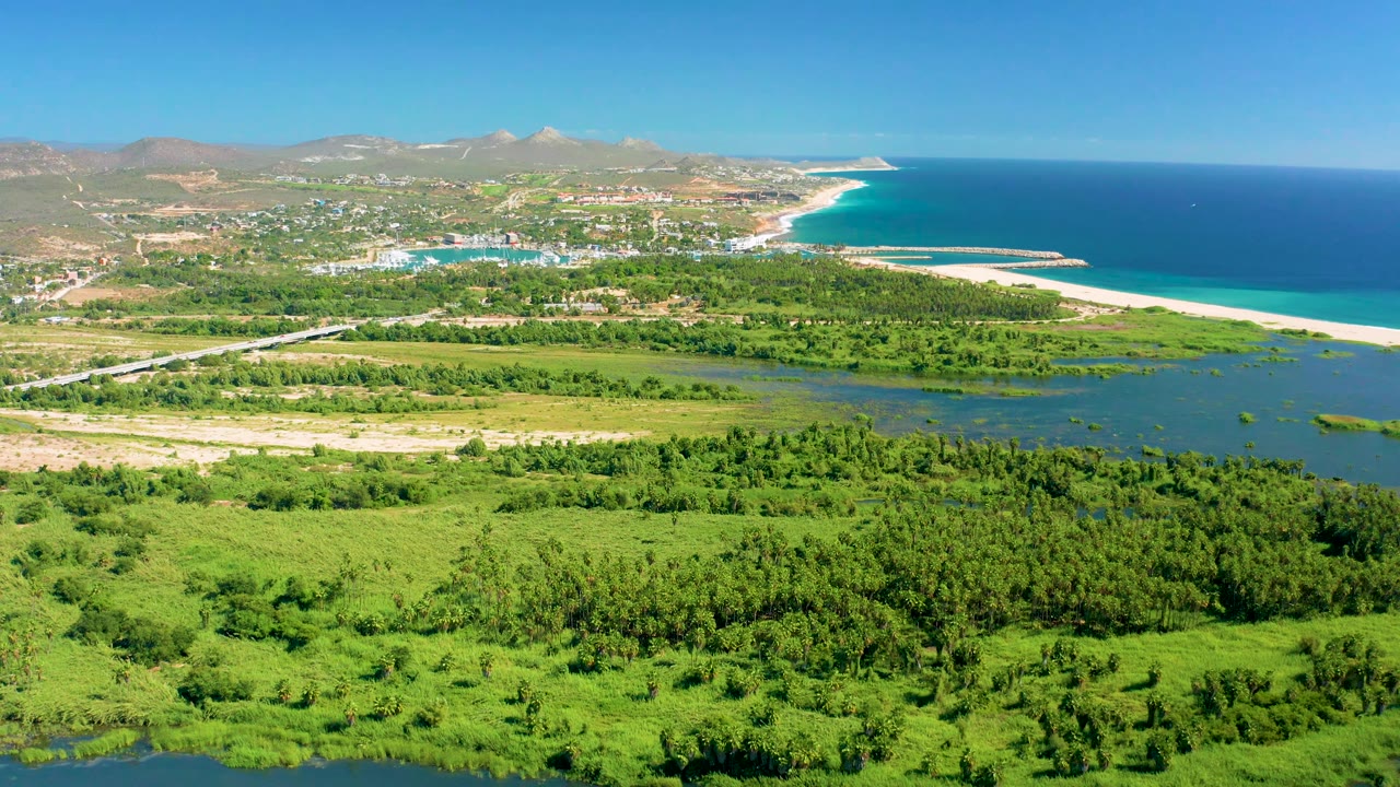 Coastal highway area with green wetlands, beach, ocean, and hills.