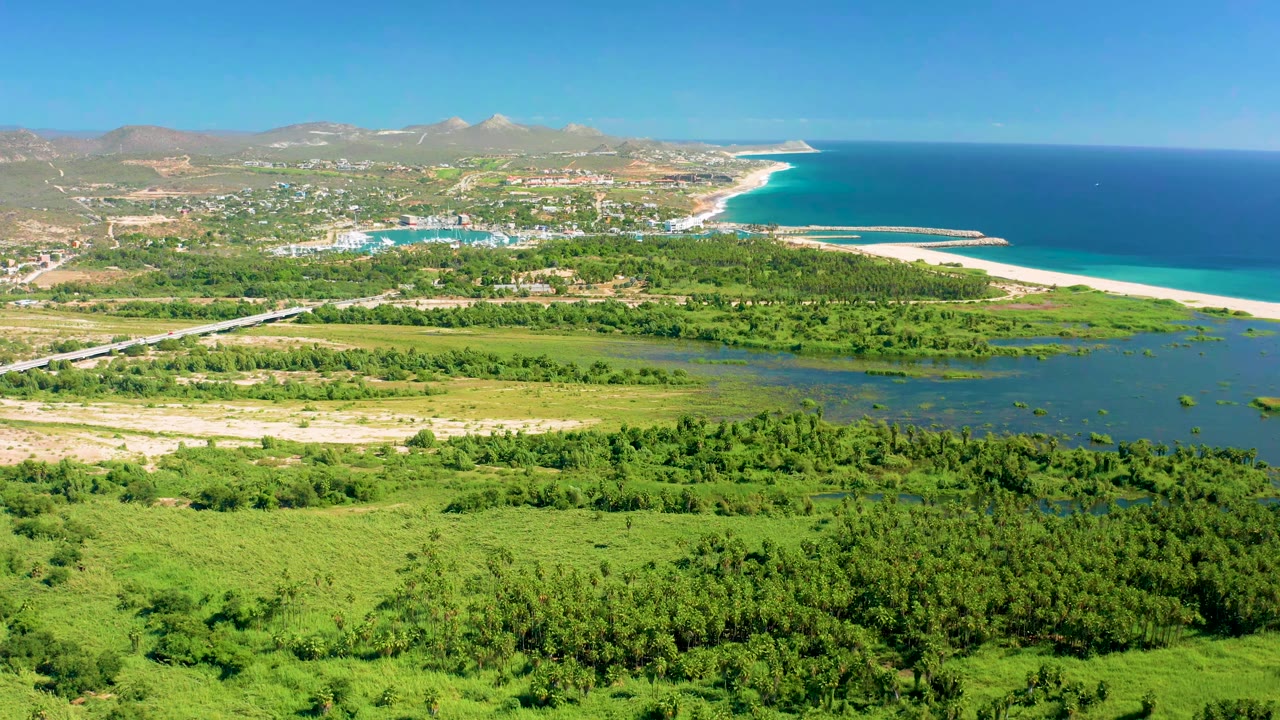 High aerial view of green coastal fields, road, beach, ocean, settlement, and mountains.