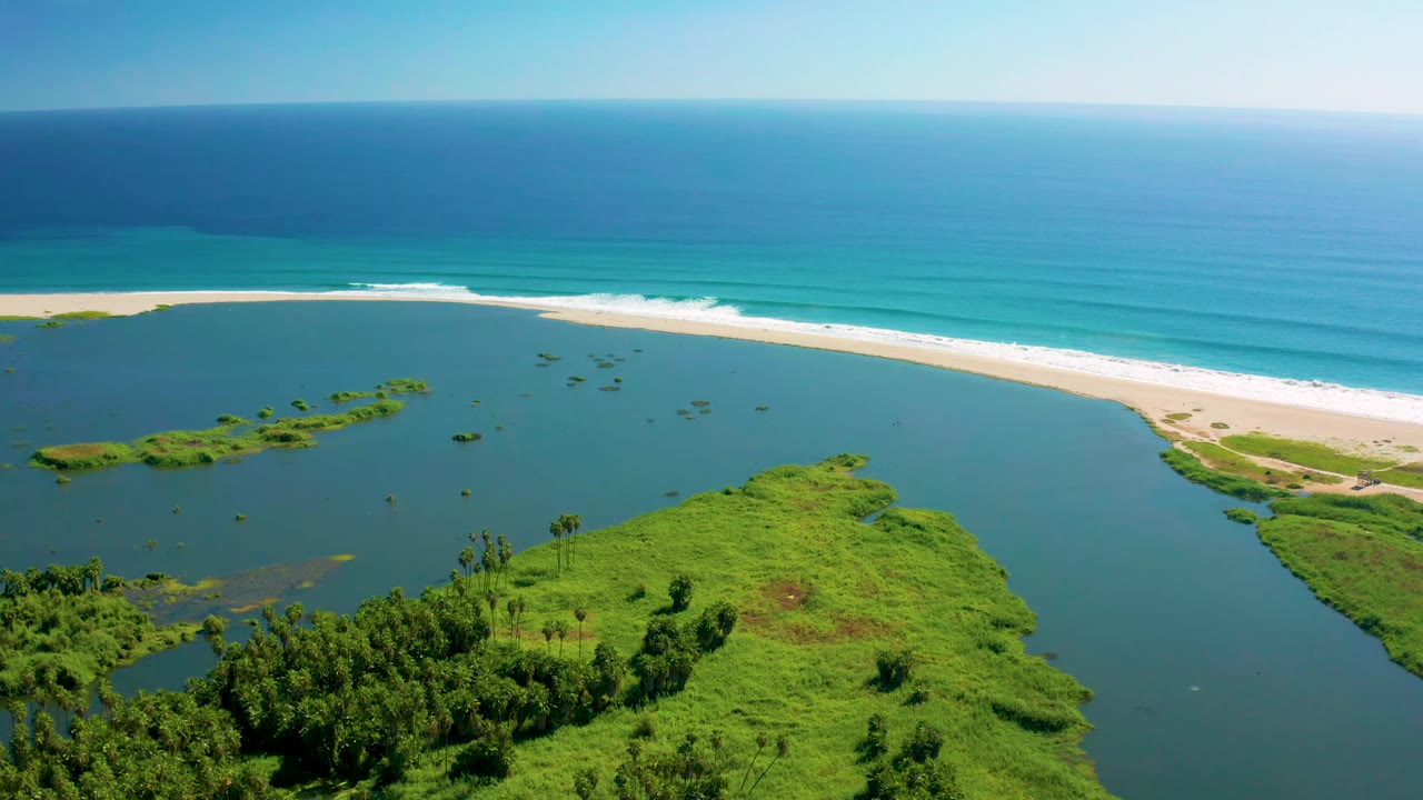 Aerial coastal lagoon with green shoreline and surf beyond a sandbar