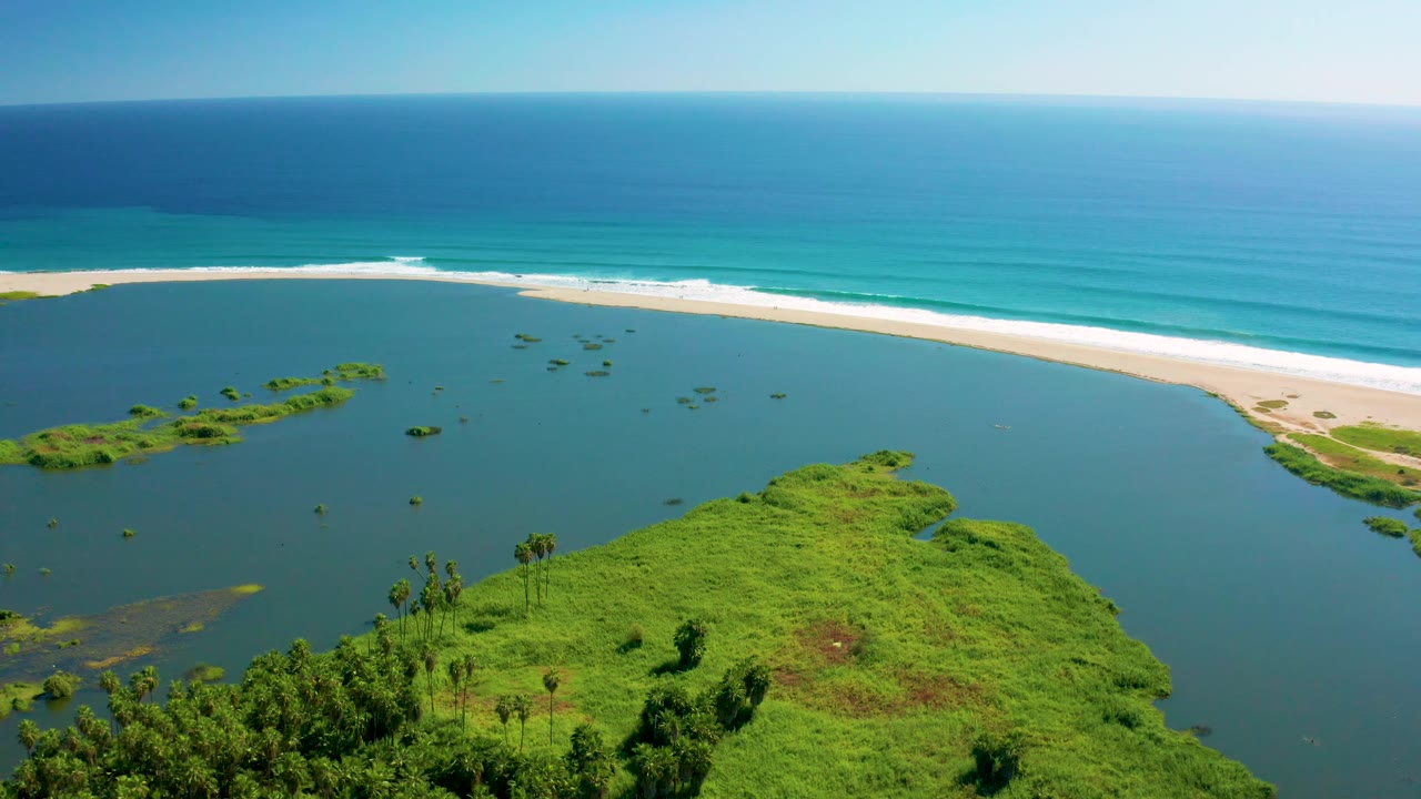 Wide aerial of lagoon water separated from ocean by a long sandy beach.