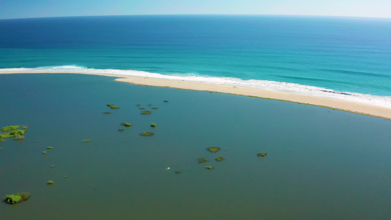 San Jose del Cabo aerial frame with lagoon water filling most of the foreground, small green patches near the left and center, a pale beach strip, and no visible people.