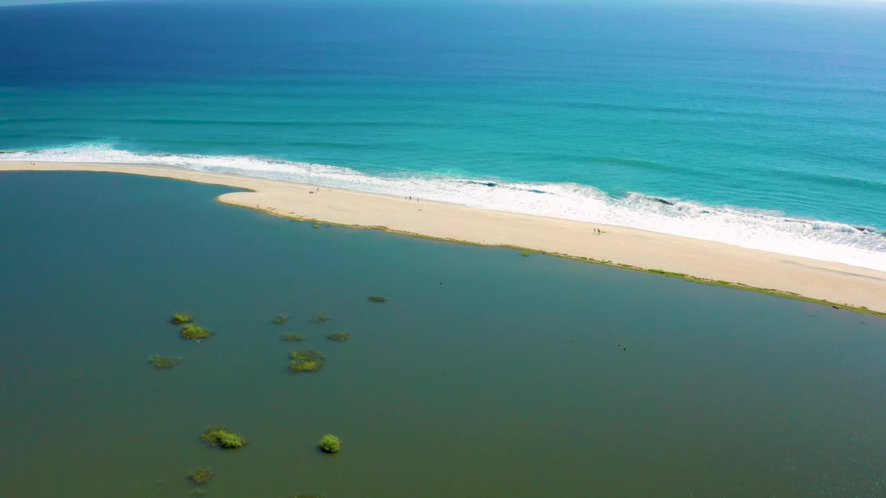 Aerial San Jose del Cabo beach frame with the sand running diagonally, white waves meeting the ocean side, and green patches in the shallow water, no visible people.