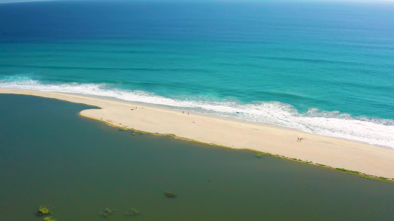 Diagonal sand beach with ocean waves above and calm green water below.