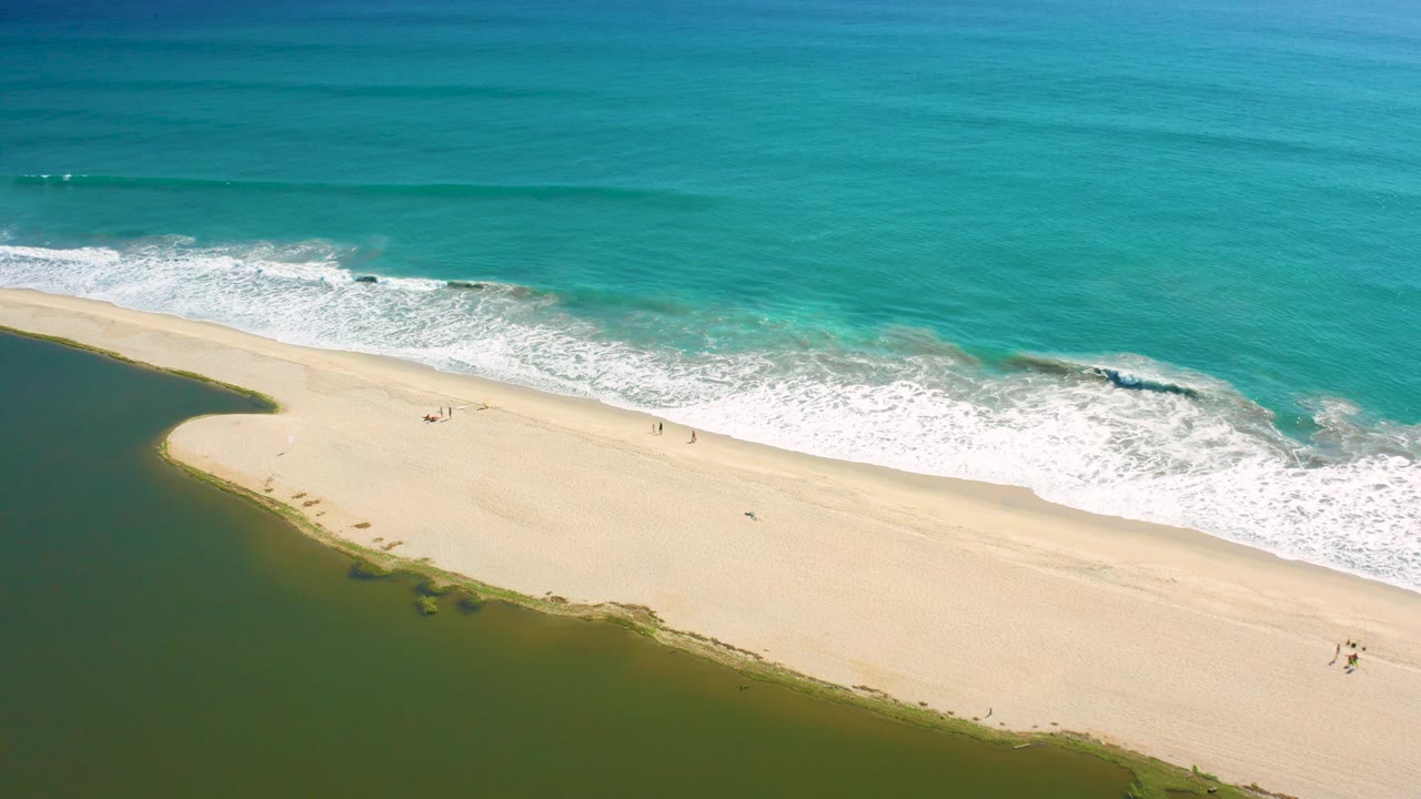Aerial view in San Jose del Cabo where a foamy wave band reaches the upper edge of the sand while the lagoon curves around the lower left side.