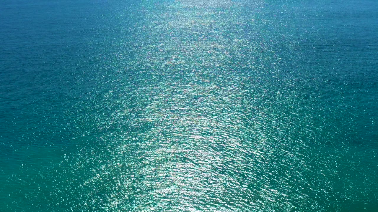 Overhead view of turquoise ocean water in San Jose del Cabo with a broad silver sunlight path near the lower center and no visible people.