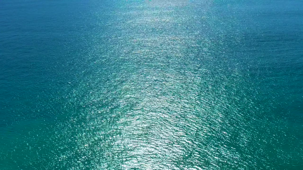 Aerial ocean surface in San Jose del Cabo shifts from deeper blue at the top to turquoise below, with a bright reflective band and no visible people.