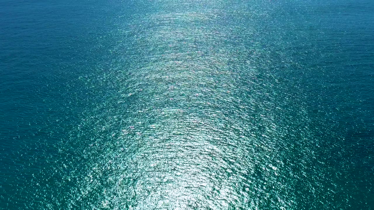 Aerial frame over San Jose Del Cabo ocean water with the sun glare forming a bright vertical path across darker blue ripples and no visible people.