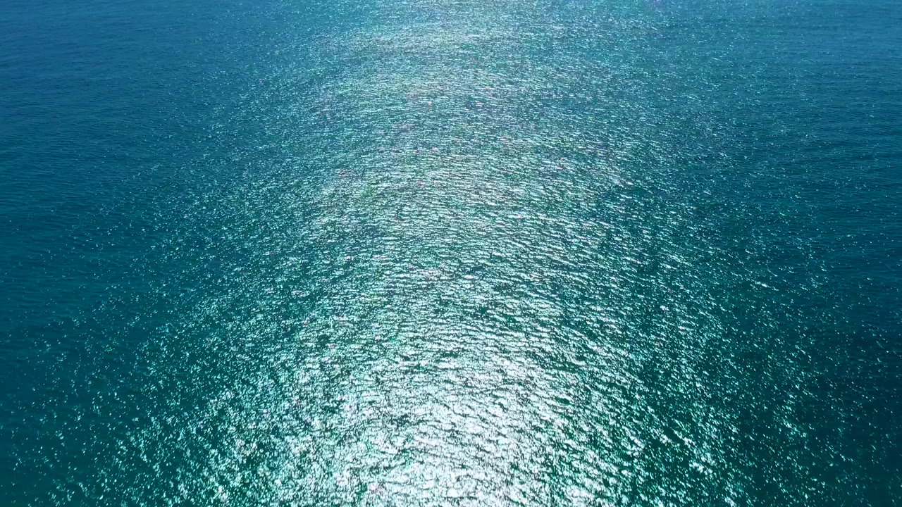 Aerial view of teal ocean in San Jose Del Cabo with dense silver-white shimmer spread across the lower half and no visible people.