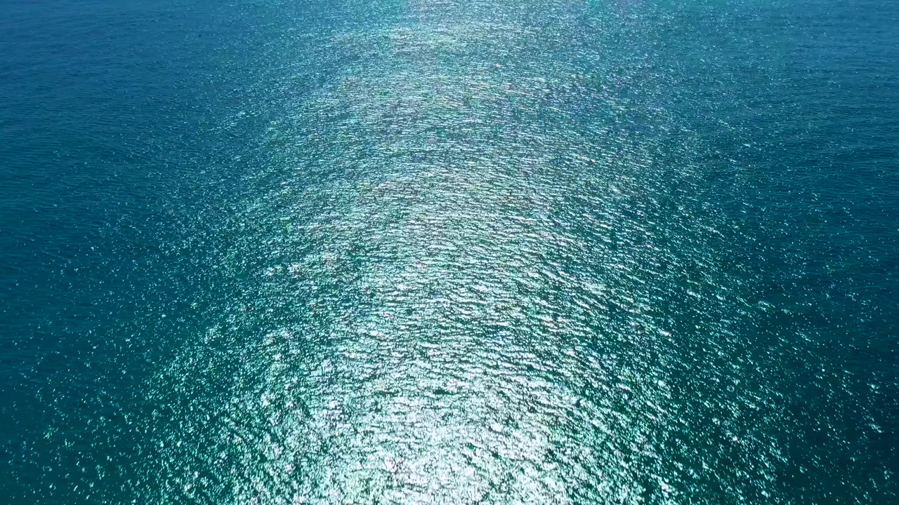 San Jose Del Cabo ocean surface seen from above, with blue green water and a concentrated sun reflection sitting low in the frame, no visible people.