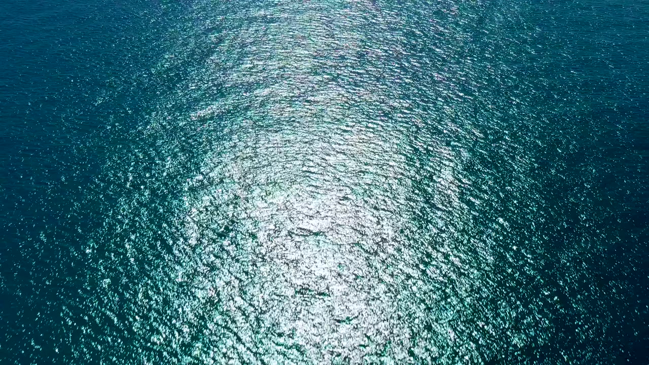 Top-down ocean frame from San Jose del Cabo with the sun reflection concentrated slightly right of center over dark teal ripples, no visible people.