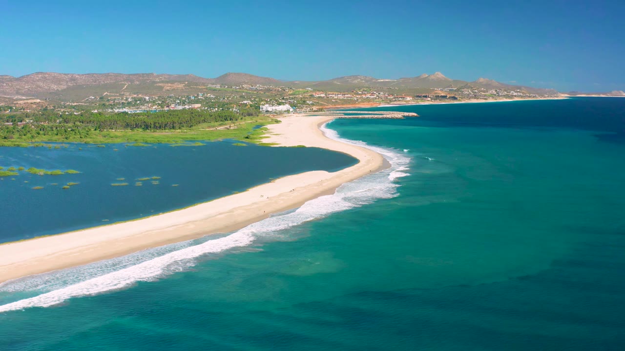 Curving sandbar with ocean waves and lagoon water.