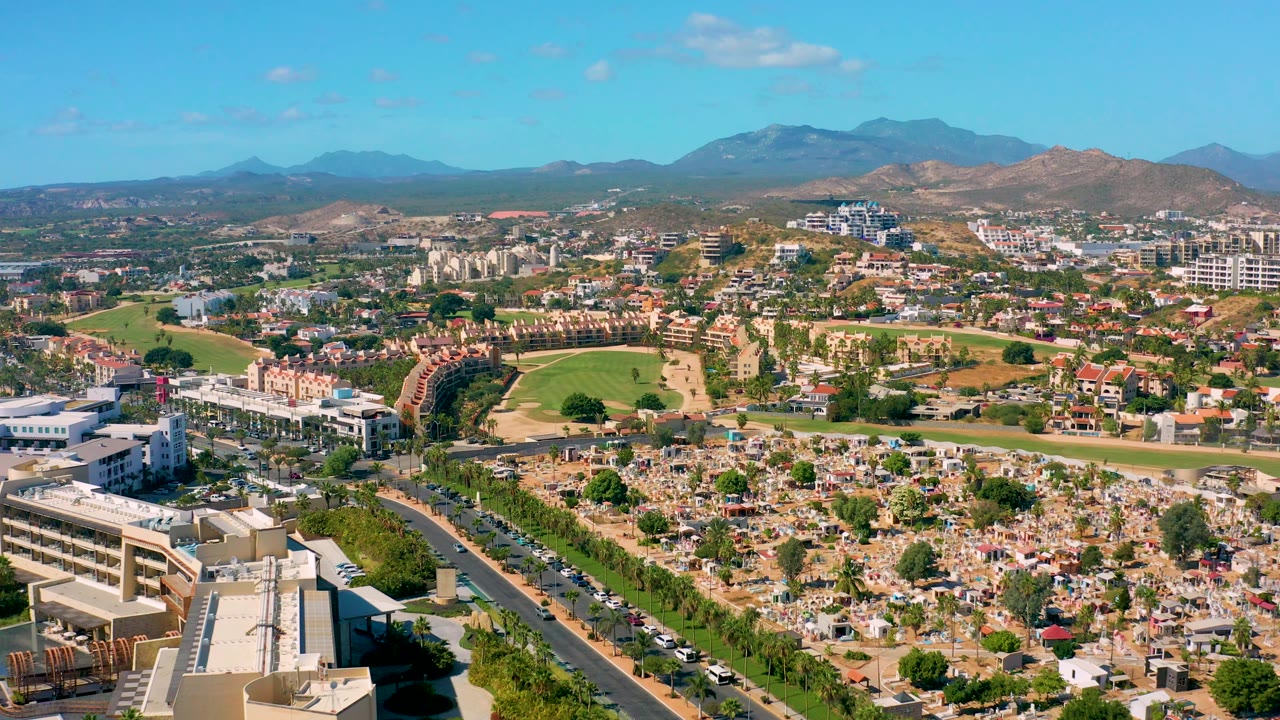 Third frame holds a wide San Jose Del Cabo aerial with the cemetery lower right, a curving road lined with cars, homes and commercial blocks, green fields, mountains, and no visible people.
