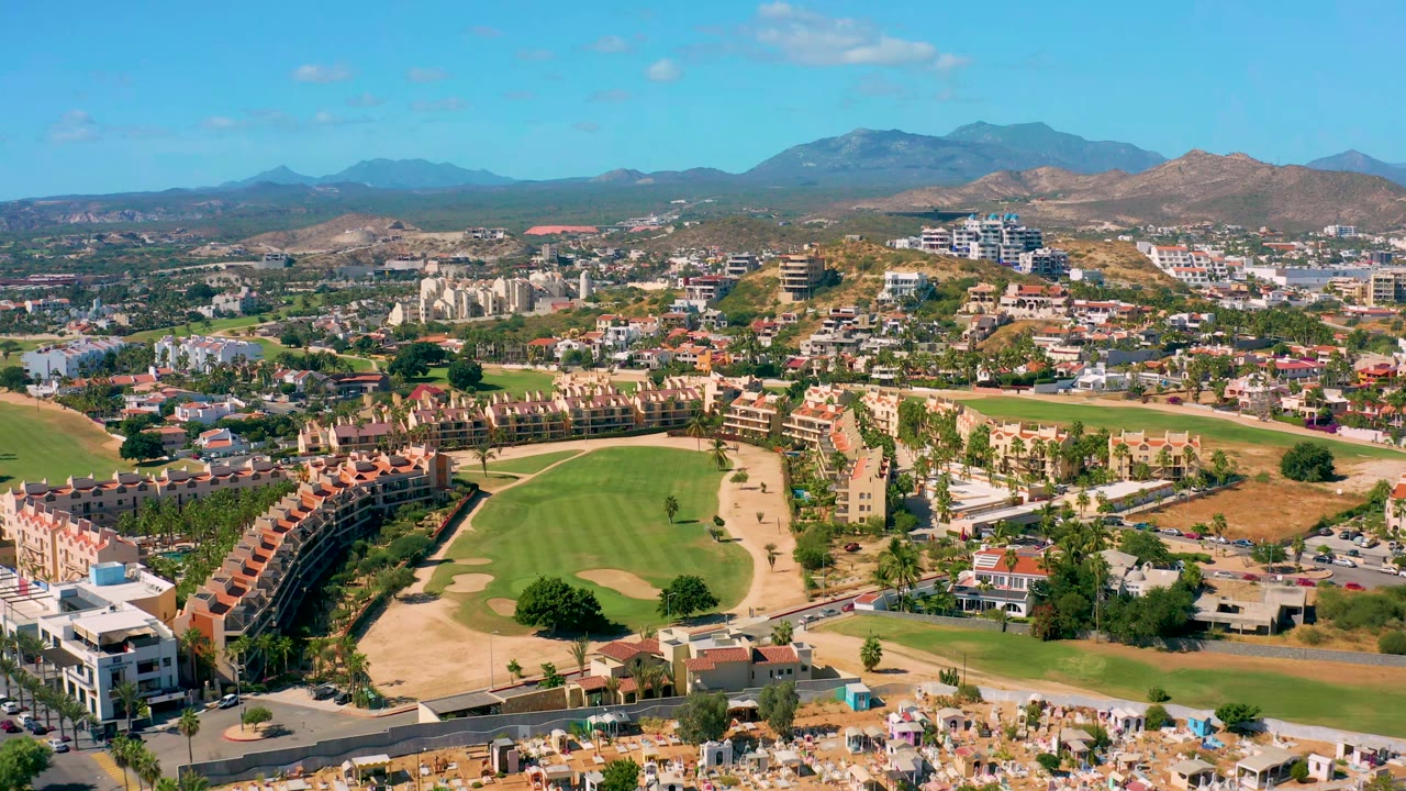 Aerial view of green fairways, tan bunkers, houses, roads, and mountains.