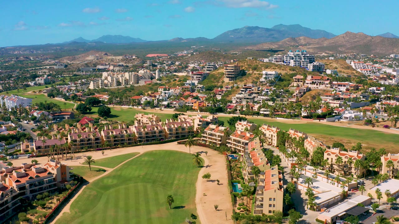 Aerial neighborhood view with golf course grass, sand, red roofs, and mountains.