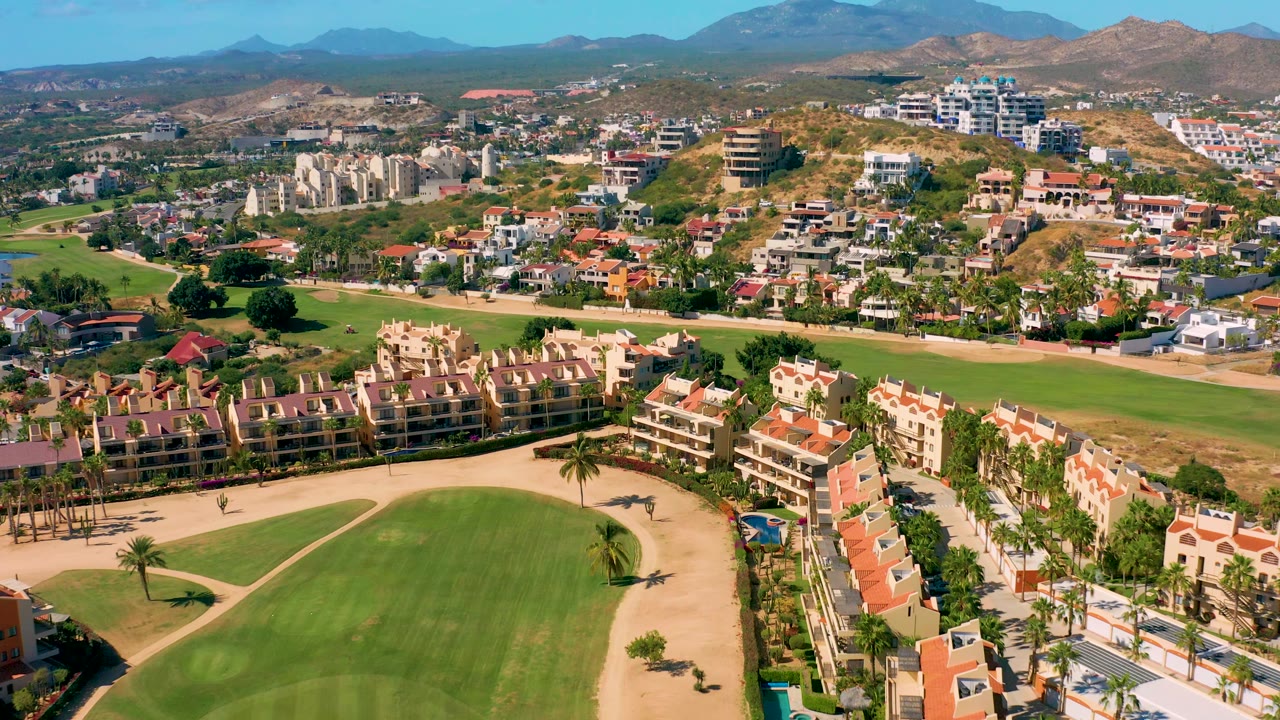Aerial view of green golf course, villas, palms, hills, and mountains.