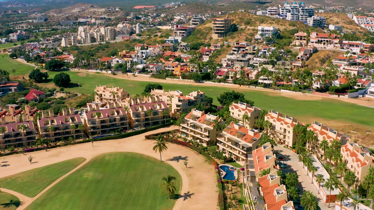 Drone view of fairway, tan residential buildings, red roofs, and hills.
