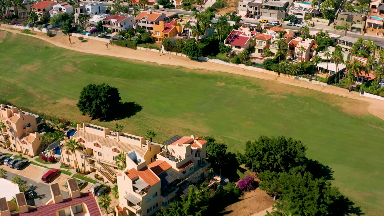 Aerial shot of field, pathway, houses, and trees in bright sun.