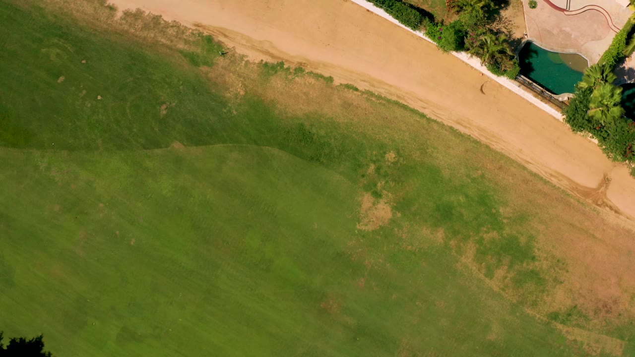 Overhead grass and sandy path with a small pool and paved patio at the upper right.