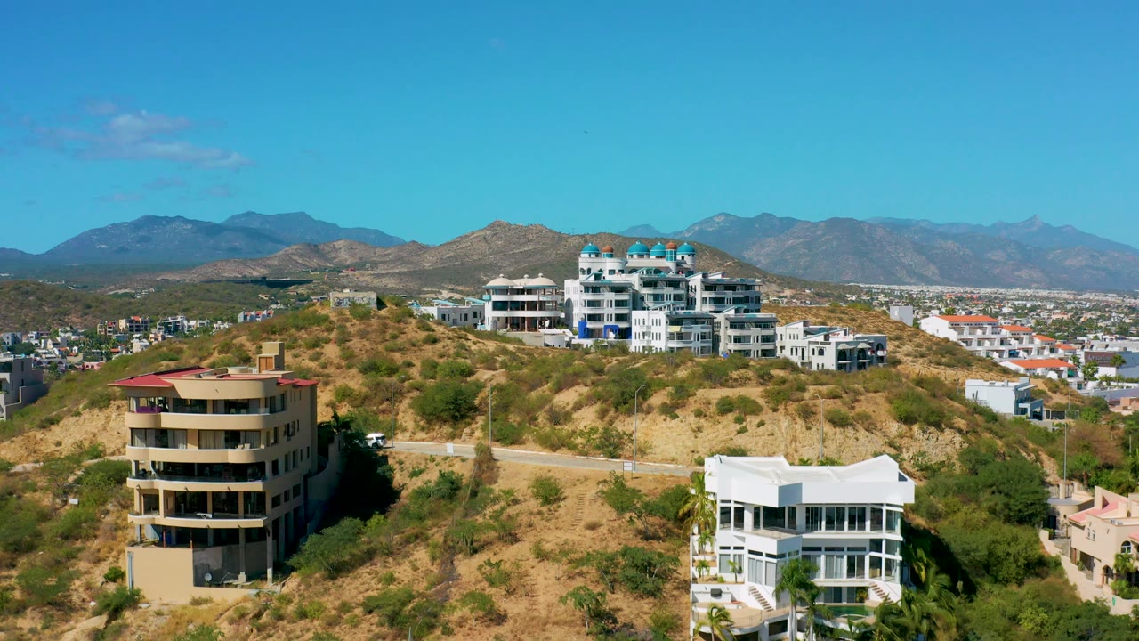 Residential hillside with white buildings, tan building, and mountain skyline.