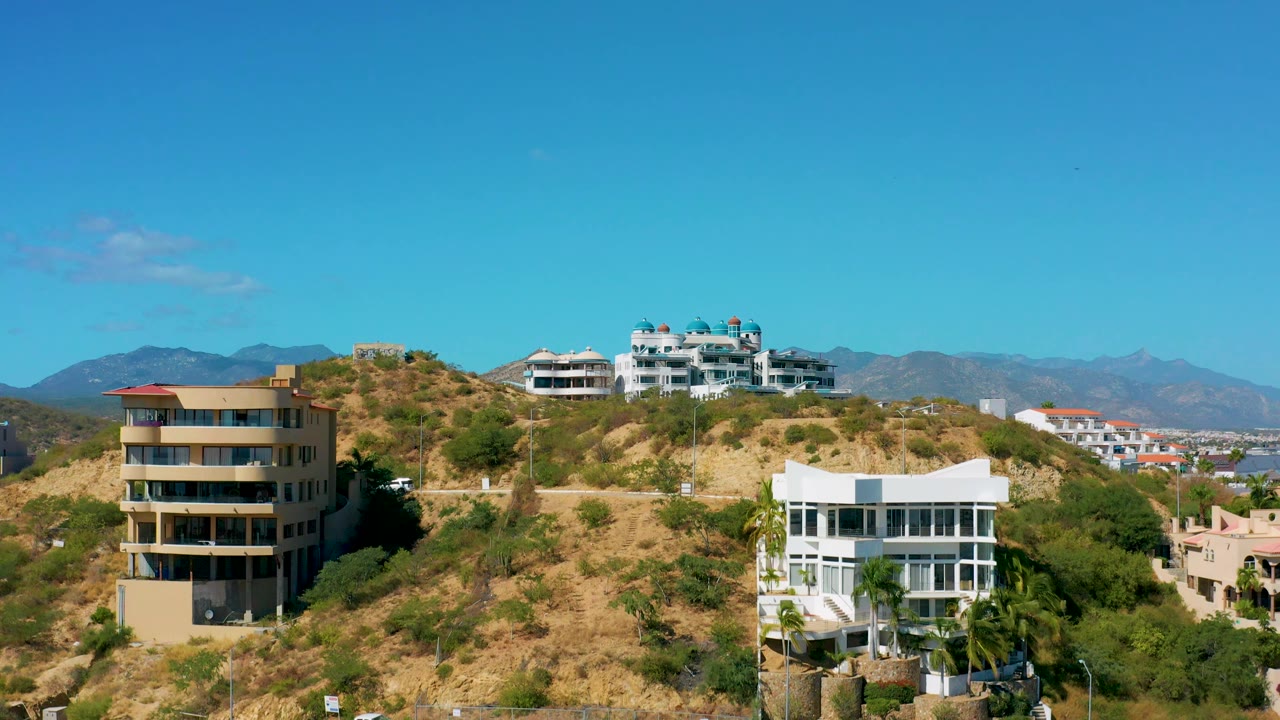 San Jose del Cabo residential hillside view with modern homes on the slope, a broad blue sky, mountain ridge in the distance, and no visible people.