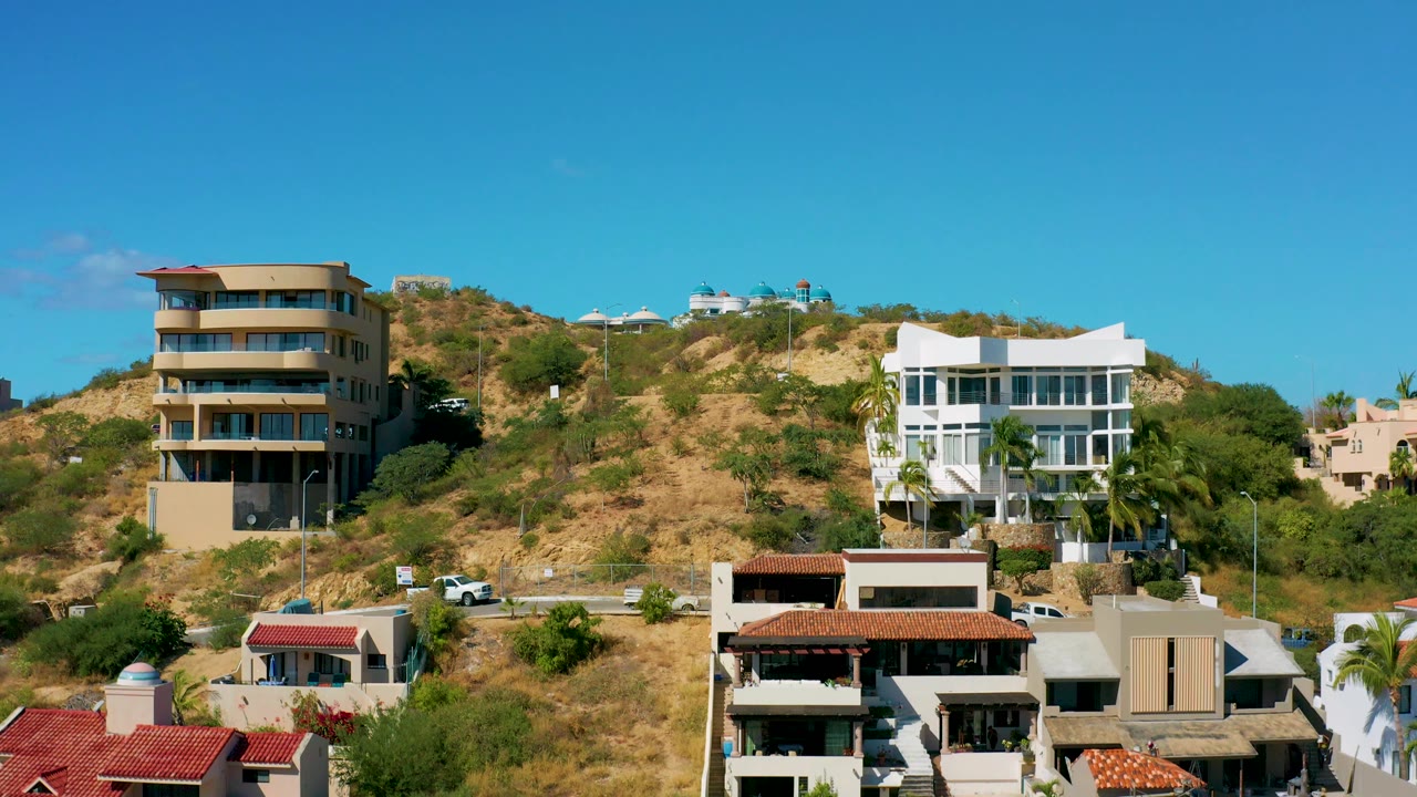 Hillside homes with red roof foreground and blue sky.