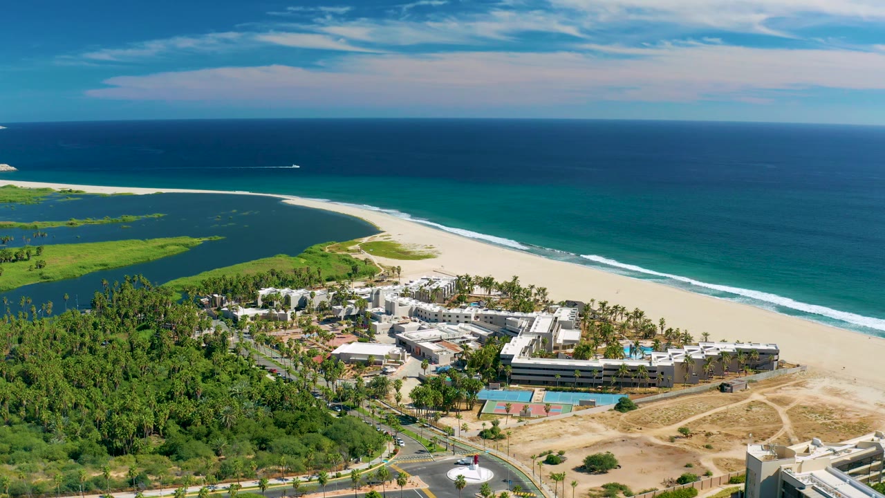 Aerial view of San Jose del Cabo coastline with ocean horizon, lagoon, sandy beach, roads, coastal development, and no visible people at 0:02.