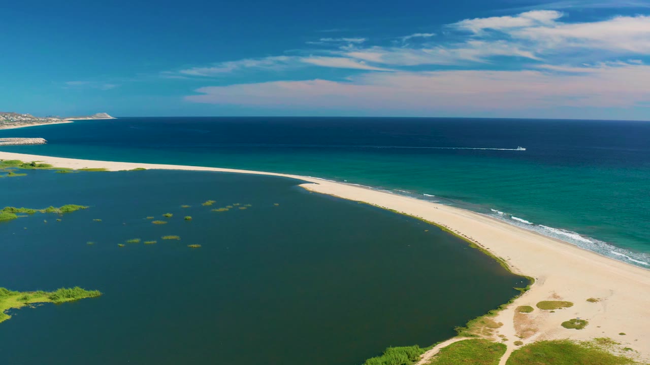 Wide drone view of lagoon water, curving sandbar, ocean, and boat wake.