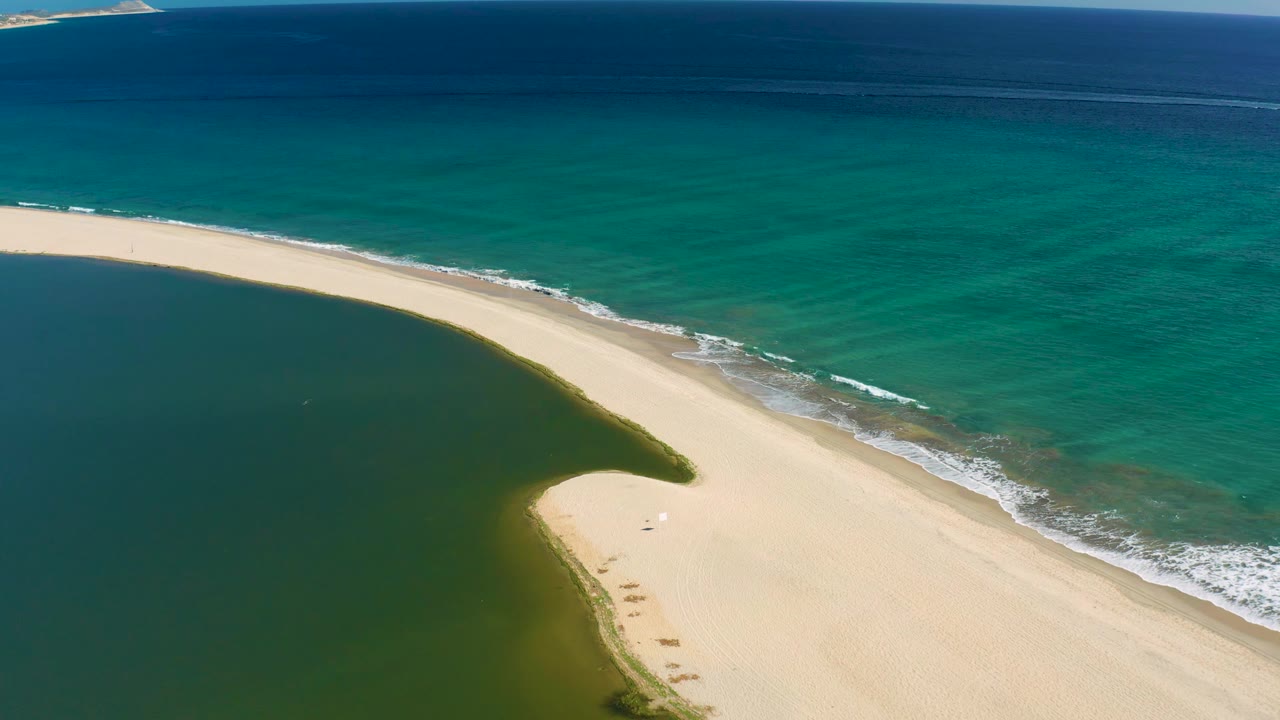 Sand spit curving between green lagoon water and turquoise surf