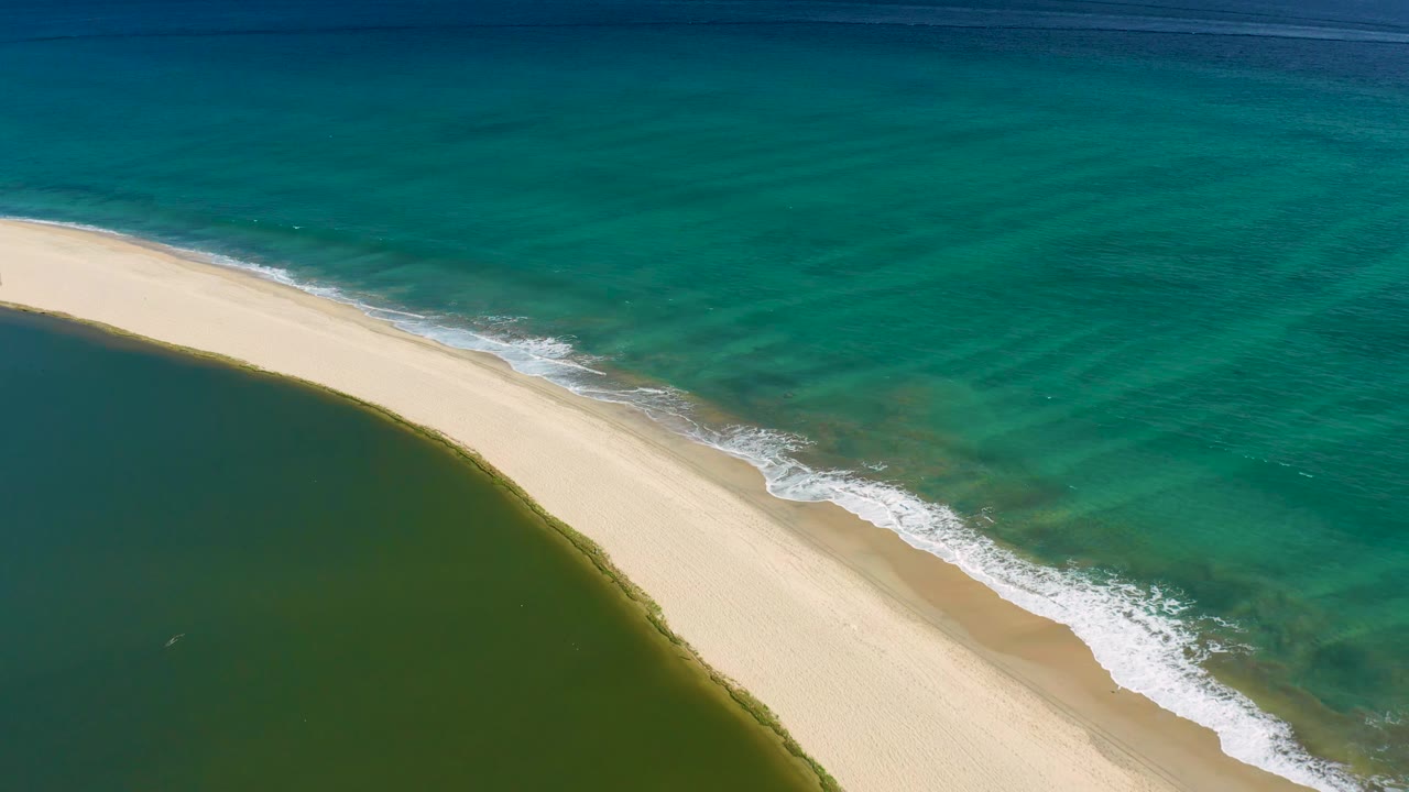 Curved beach with surf foam beside turquoise ocean and green lagoon