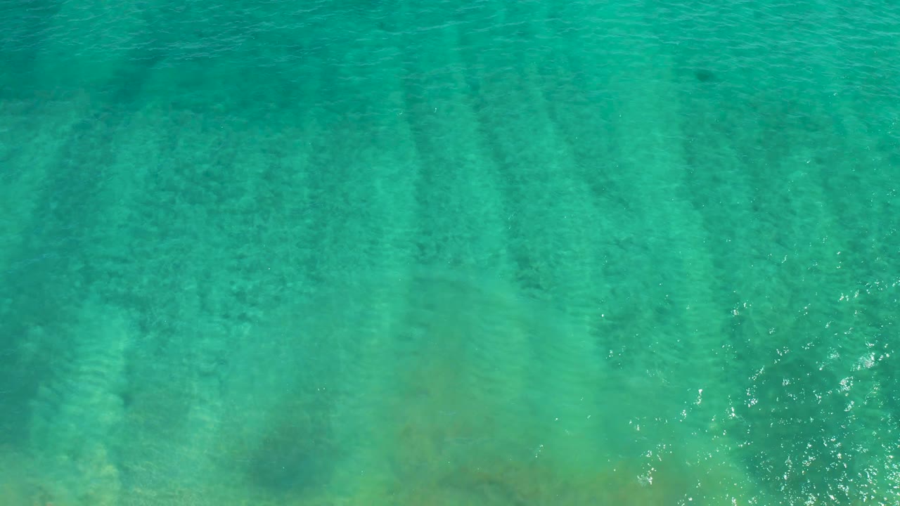 Clear teal water fills the frame in San Jose del Cabo, with mottled seabed shapes and small highlights on the surface, no visible people.