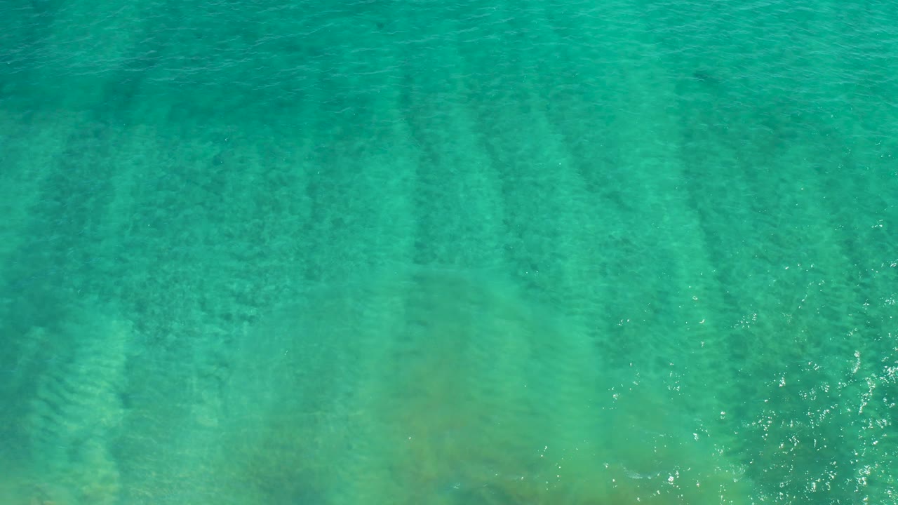 Aerial frame over turquoise water in San Jose del Cabo showing faint dark patches beneath a lightly rippled surface, no visible people.
