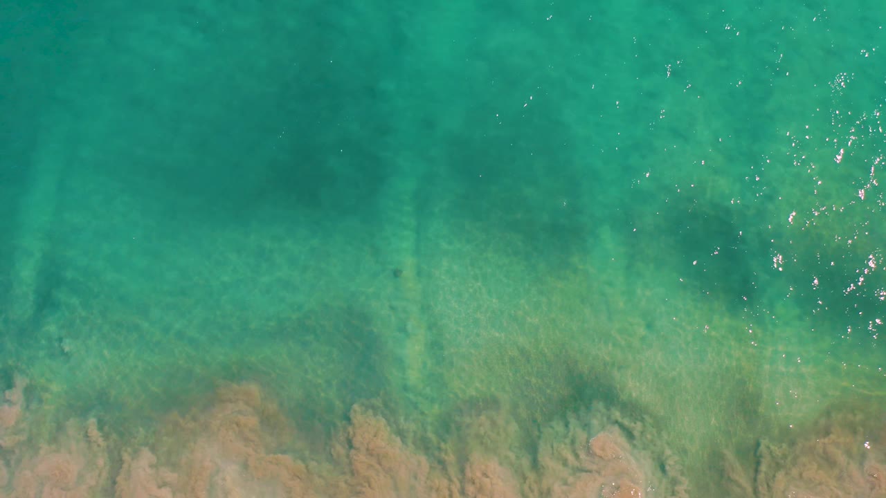 Sunlit turquoise water over a shallow sandy bottom in San Jose del Cabo, with bright surface highlights and no visible people.