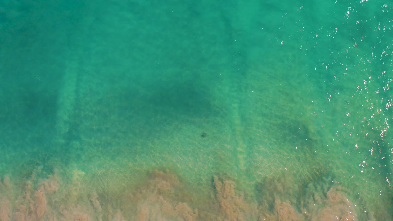 Overhead view of turquoise shallow water in San Jose Del Cabo with tan rocky seabed visible below the surface and no visible people.