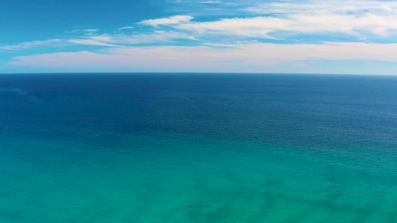 One second into the San Jose del Cabo clip, the shallow turquoise foreground water shows faint wave texture below a broad dark-blue ocean band and clouded sky, with no visible people.