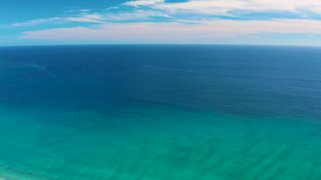 A high coastal view in San Jose del Cabo shows open blue ocean meeting a cloud-streaked sky above bright turquoise nearshore water, with no visible people.