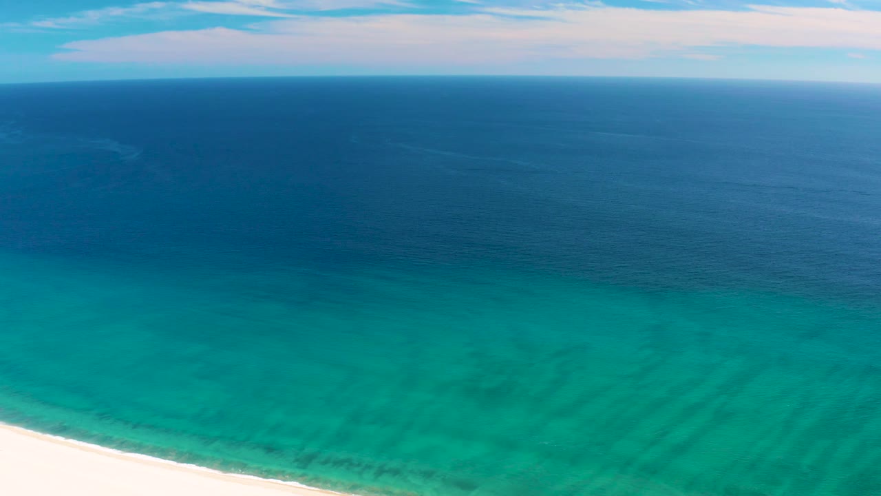 Aerial beach edge with clear green-blue water and calm open ocean.