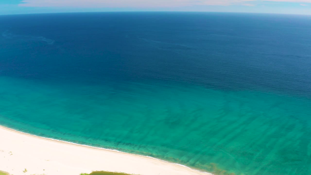 High view of empty white beach and turquoise coastal water.