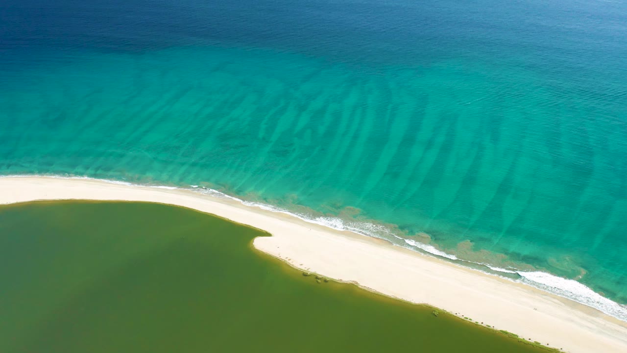 Curved sandy shoreline between ocean and lagoon.