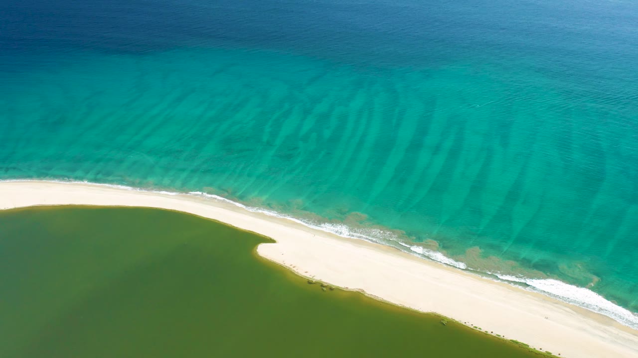 Aerial San Jose Del Cabo view with gentle white foam along the sandy beach and clear turquoise water showing subtle ripples, with no visible people.