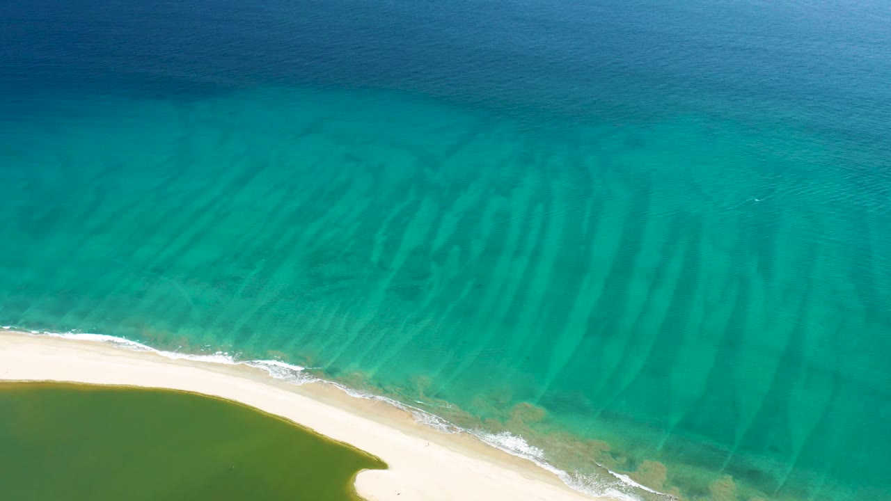 Aerial view over San Jose del Cabo shoreline with the sand curve slightly lower in frame, green water near shore, turquoise water offshore, and no visible people.