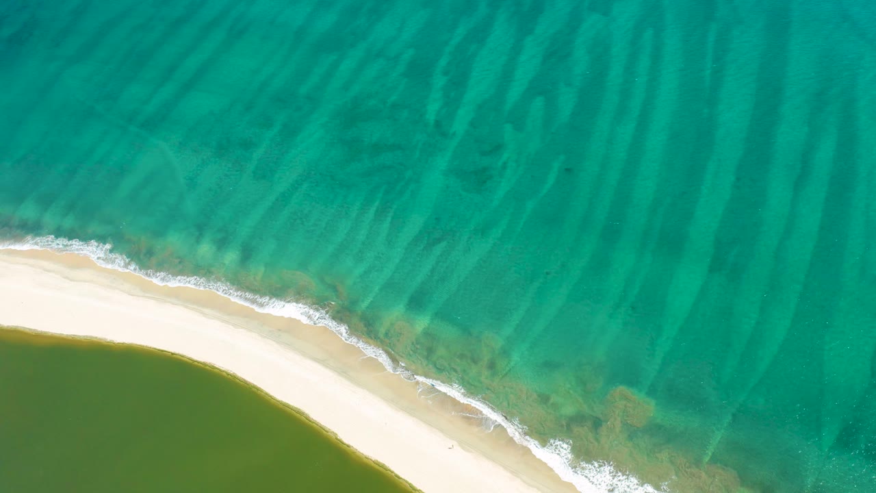 Foamy shore break runs along sand between ocean and lagoon.