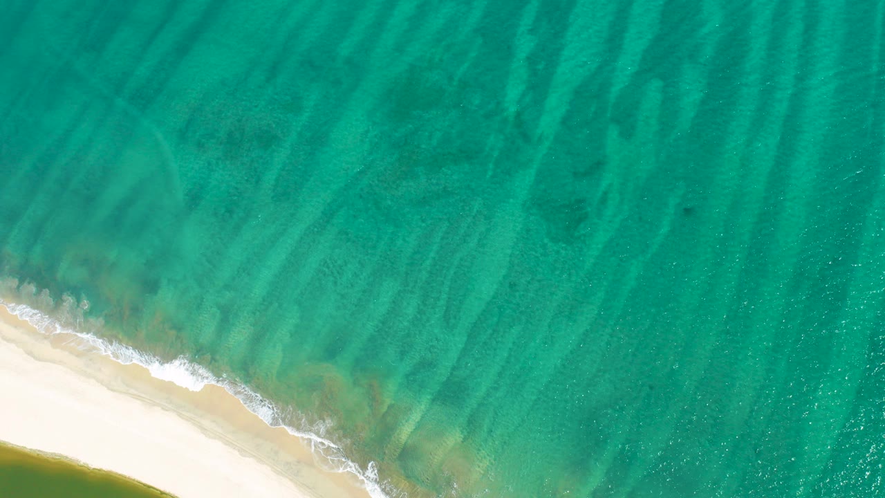 Turquoise ocean water meets pale sand with a thin line of surf foam.