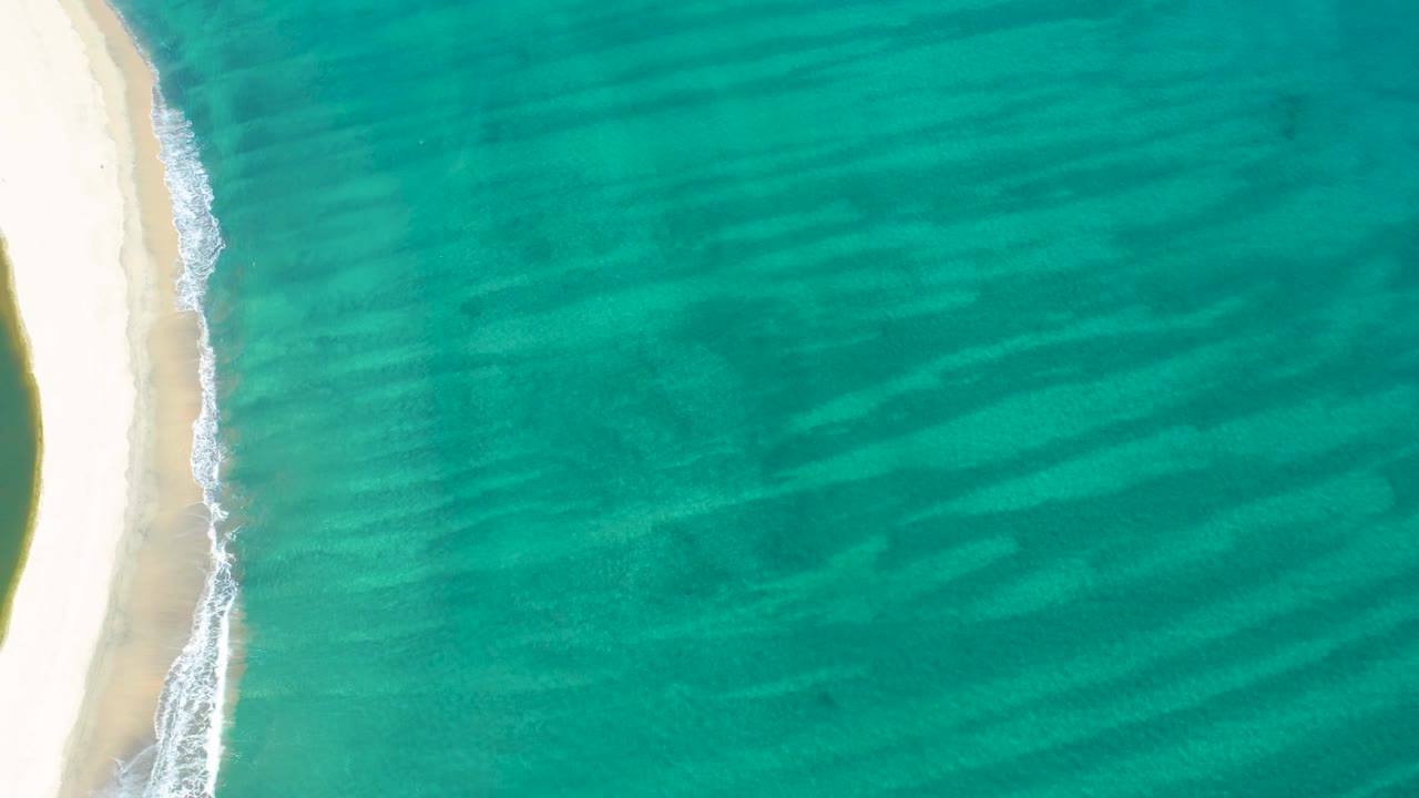 San Jose del Cabo shoreline appears as a vertical pale sand band on the left with calm turquoise sea extending rightward and no visible people.
