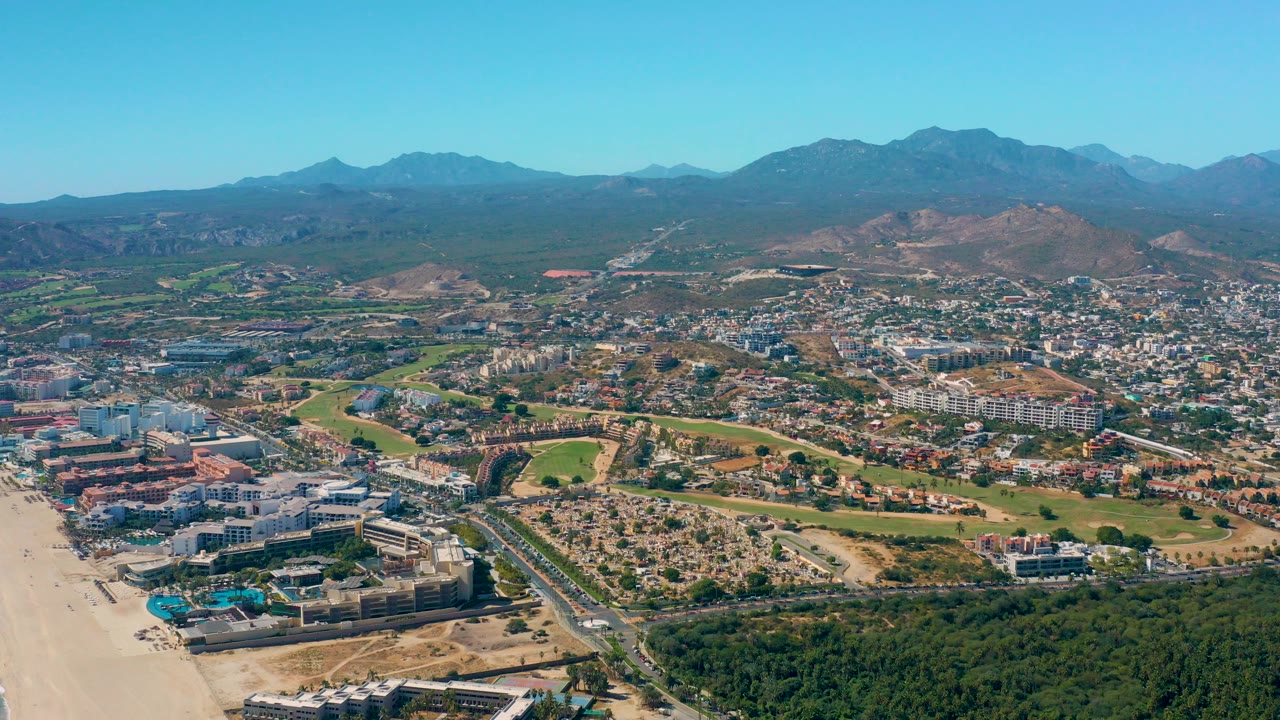 Aerial view of beach, coastal buildings, city blocks, hills, and mountains.