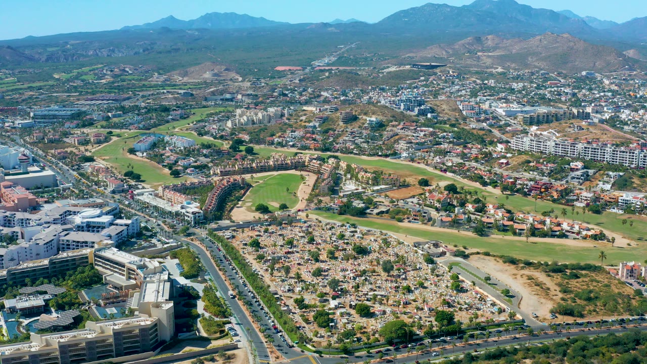 Aerial panorama of city streets, buildings, golf course, and distant mountains.