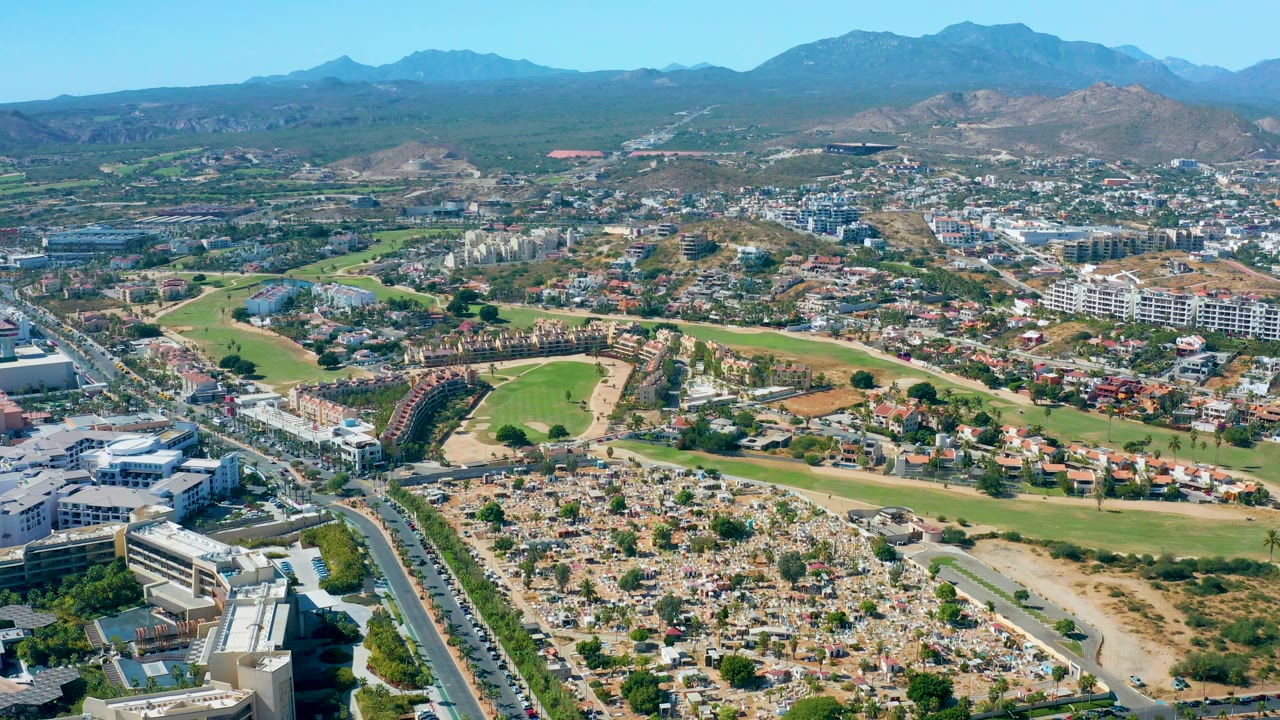 Aerial cityscape with road traffic, houses, open land, and mountains.